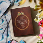 Brown book titled 'Bonestone & Earthflesh Tarot' with tarot cards and flowers on a light surface