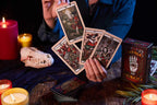 Person holding tarot cards with candles and a skull on a dark surface