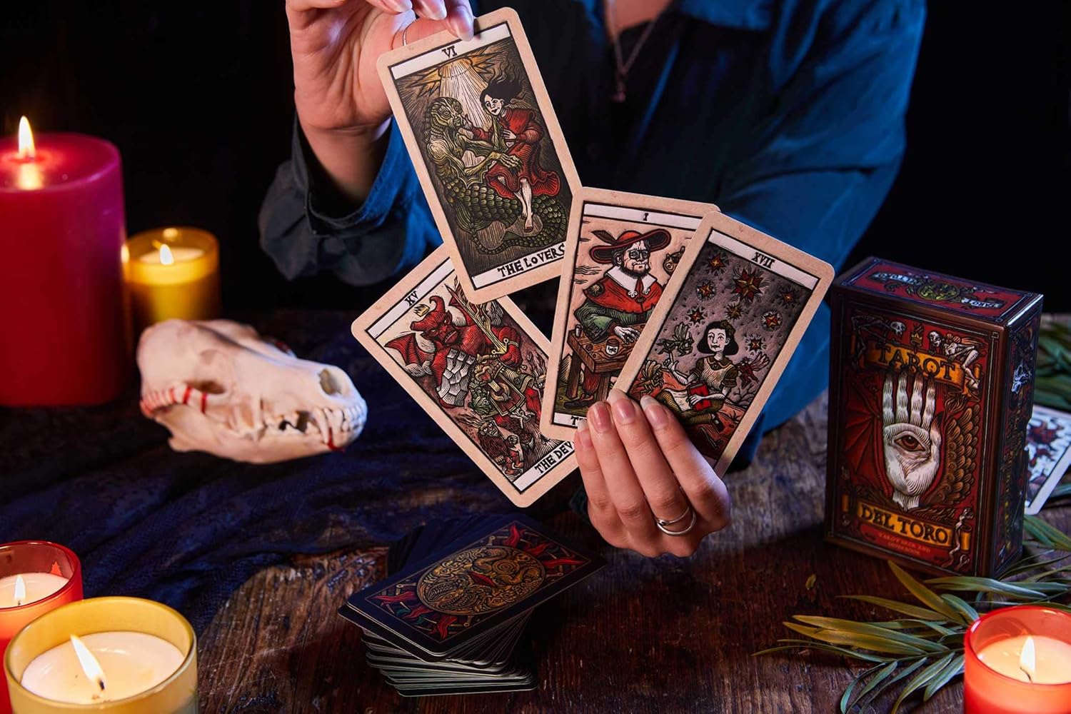 Person holding tarot cards with candles and a skull on a dark surface