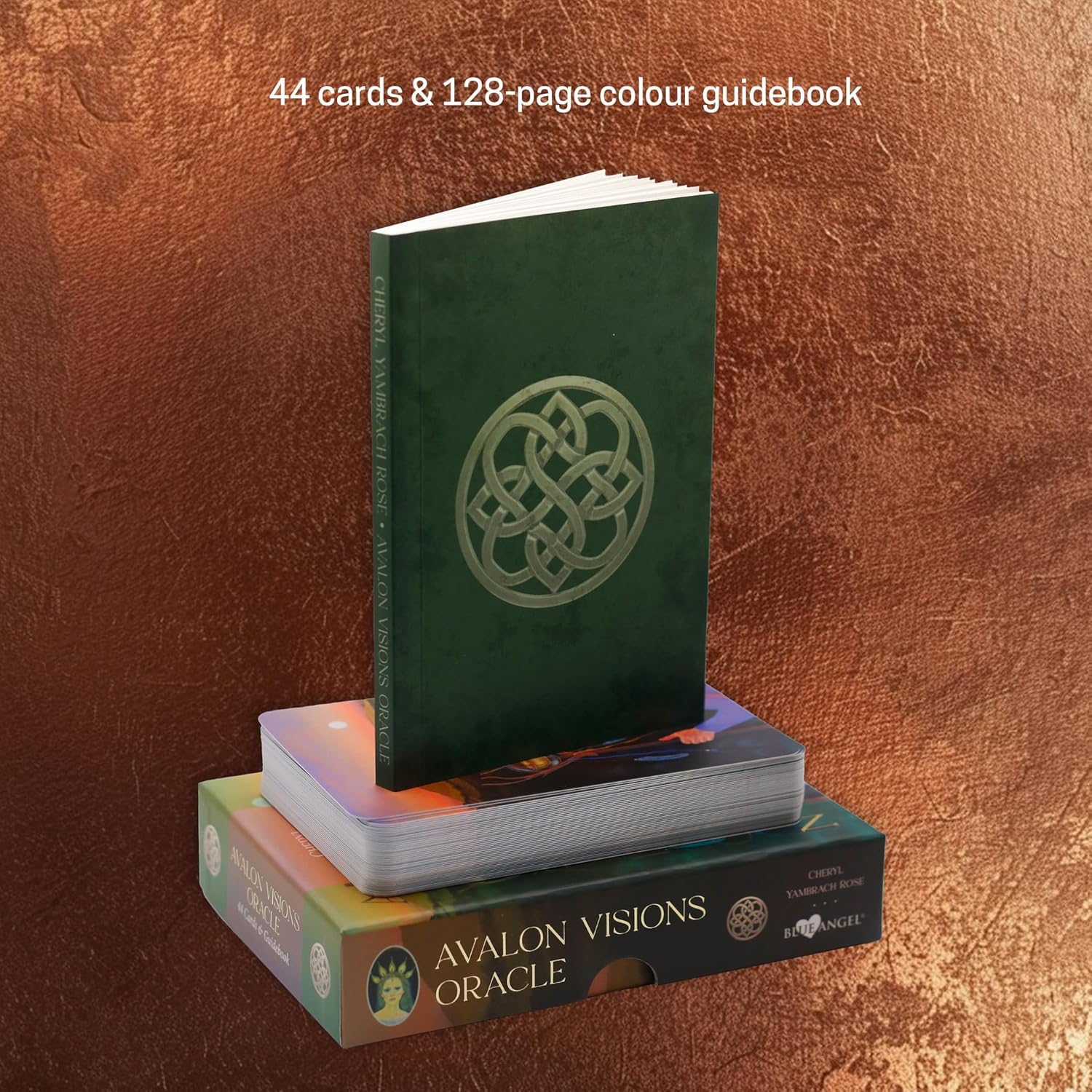Green book with a symbol on the cover and a deck of cards titled 'Avalon Visions Oracle' on a brown textured background.