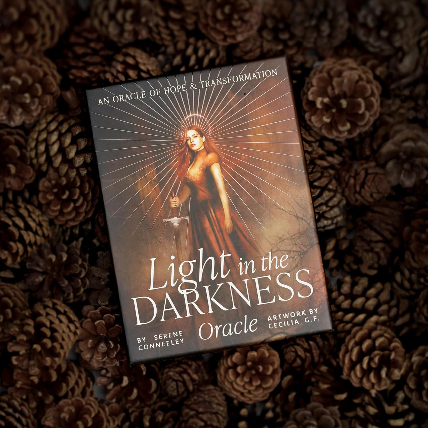 Card titled 'Light in the Darkness Oracle' on a background of pine cones