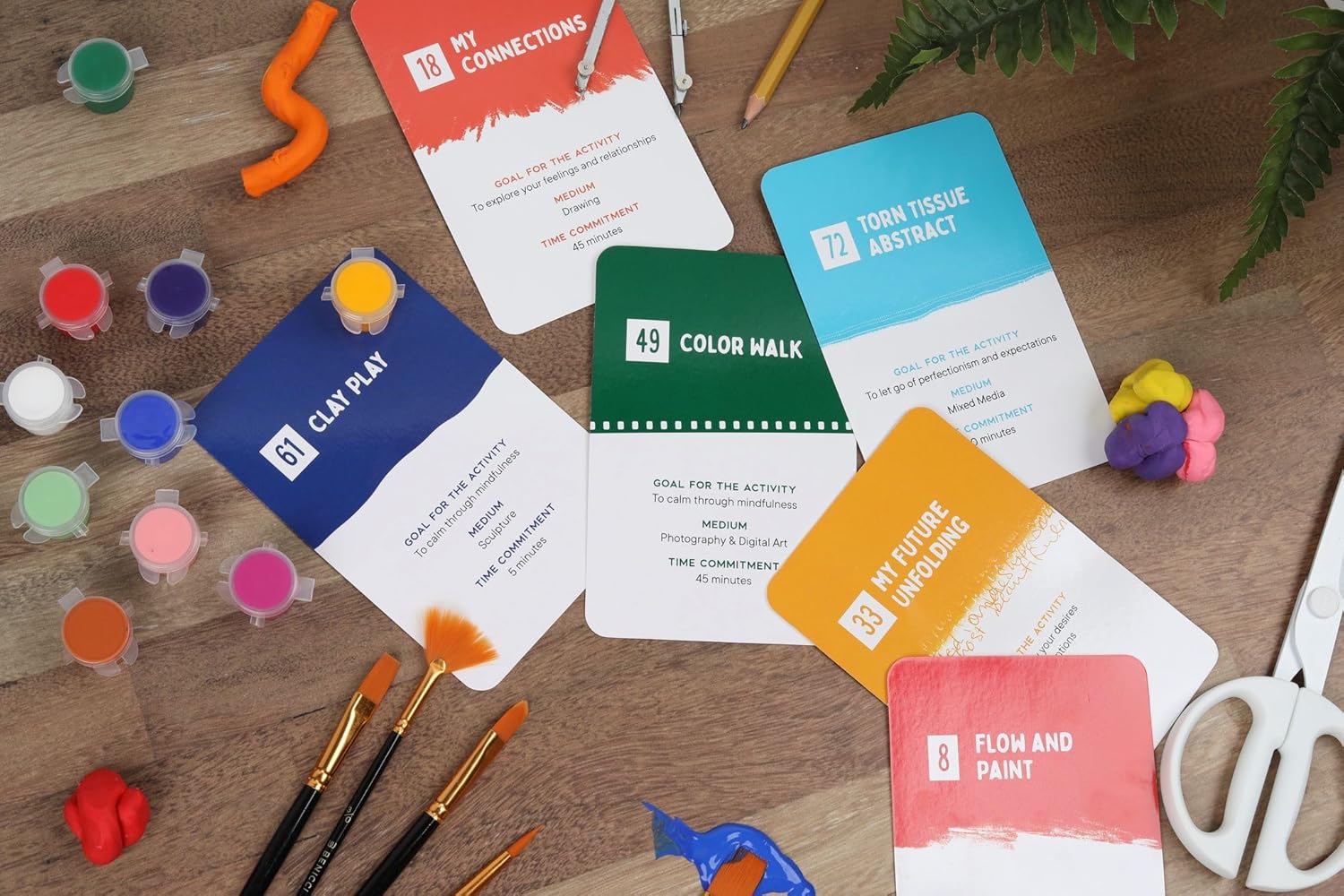 Colorful art supplies including paint, brushes, and color swatch cards on a wooden surface.