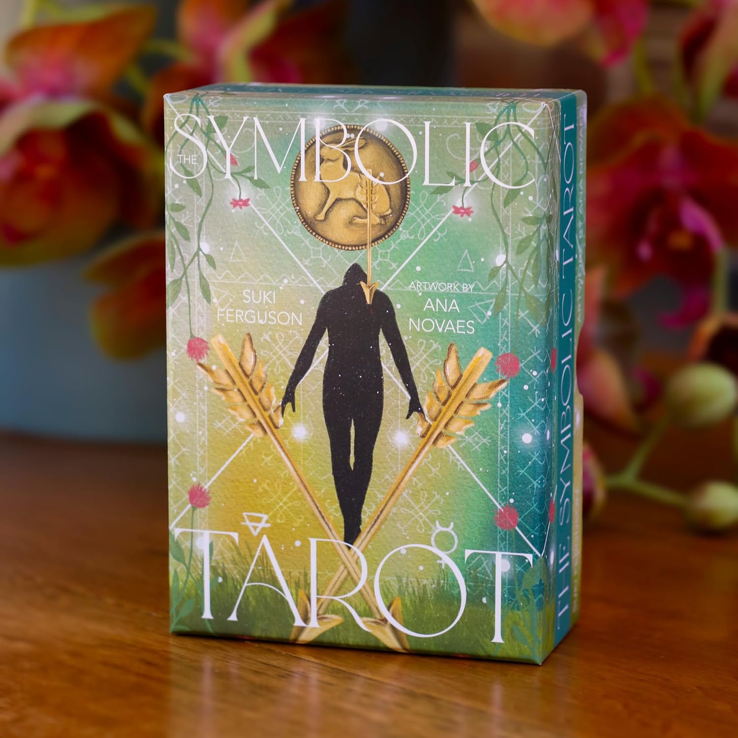 Tarot card box with symbolic design on a wooden surface with flowers in the background