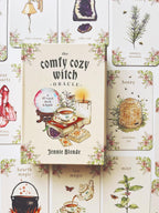The front cover of 'The Comfy Cozy Witch Oracle' deck box is centered, surrounded by illustrated oracle cards with vintage-style drawings of crystals, herbs, a beehive, a kettle, and tea accessories on a warm cream background.