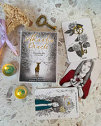 Alasha Oracle book with tarot cards on a textured surface with candles and dried flowers.