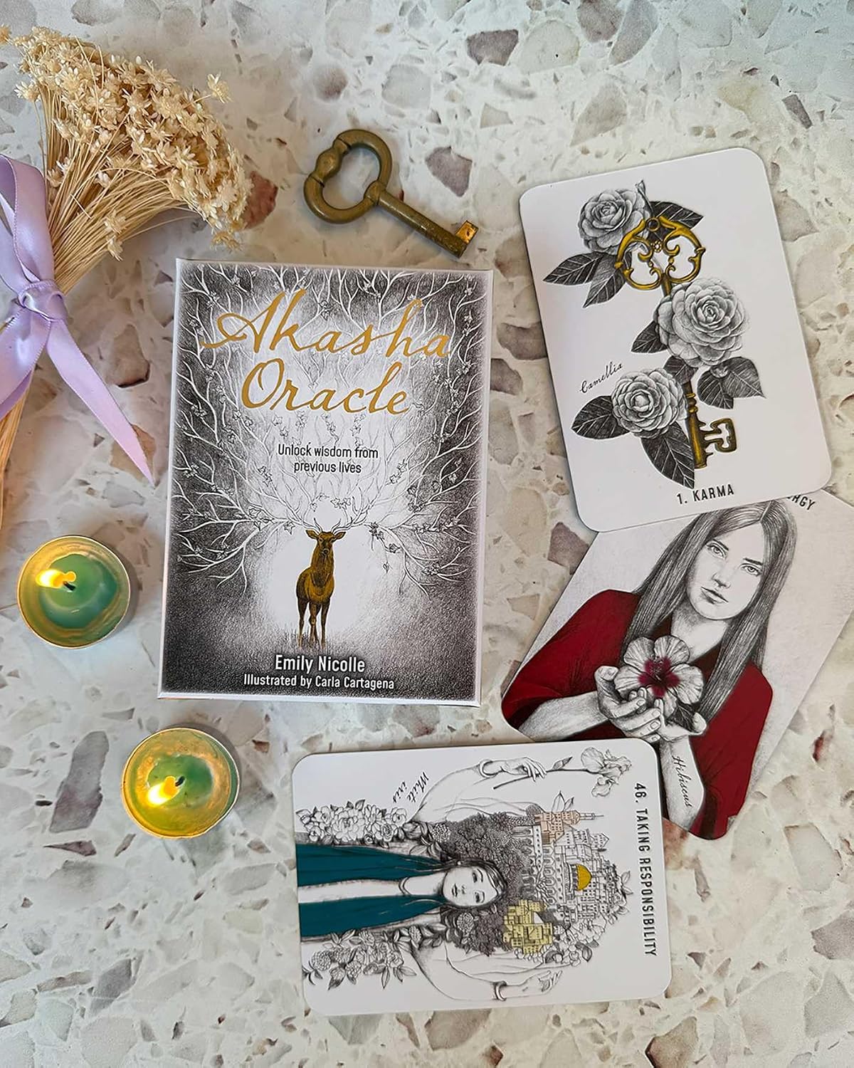 Alasha Oracle book with tarot cards on a textured surface with candles and dried flowers.
