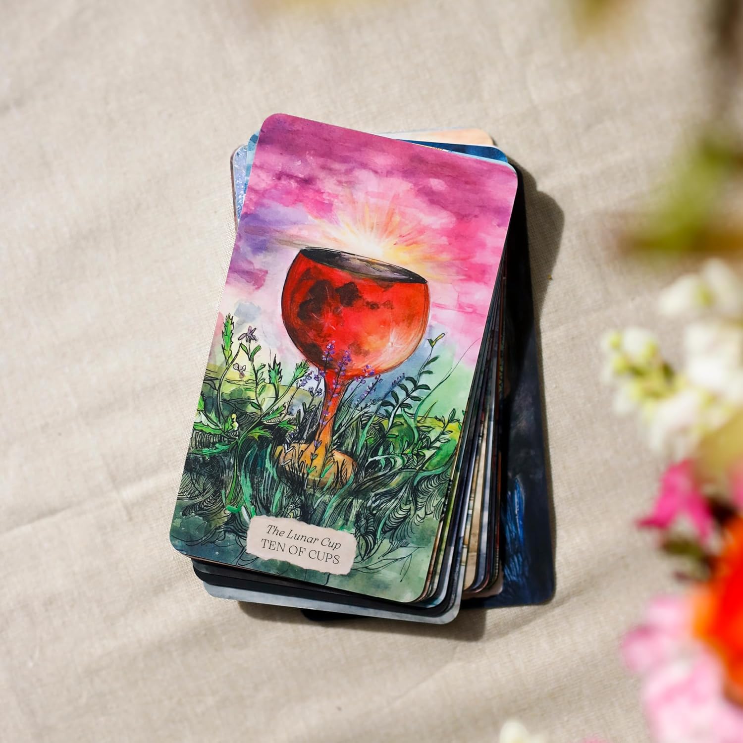 Card from a tarot deck with a colorful design of a red cup and nature elements on a textured surface.