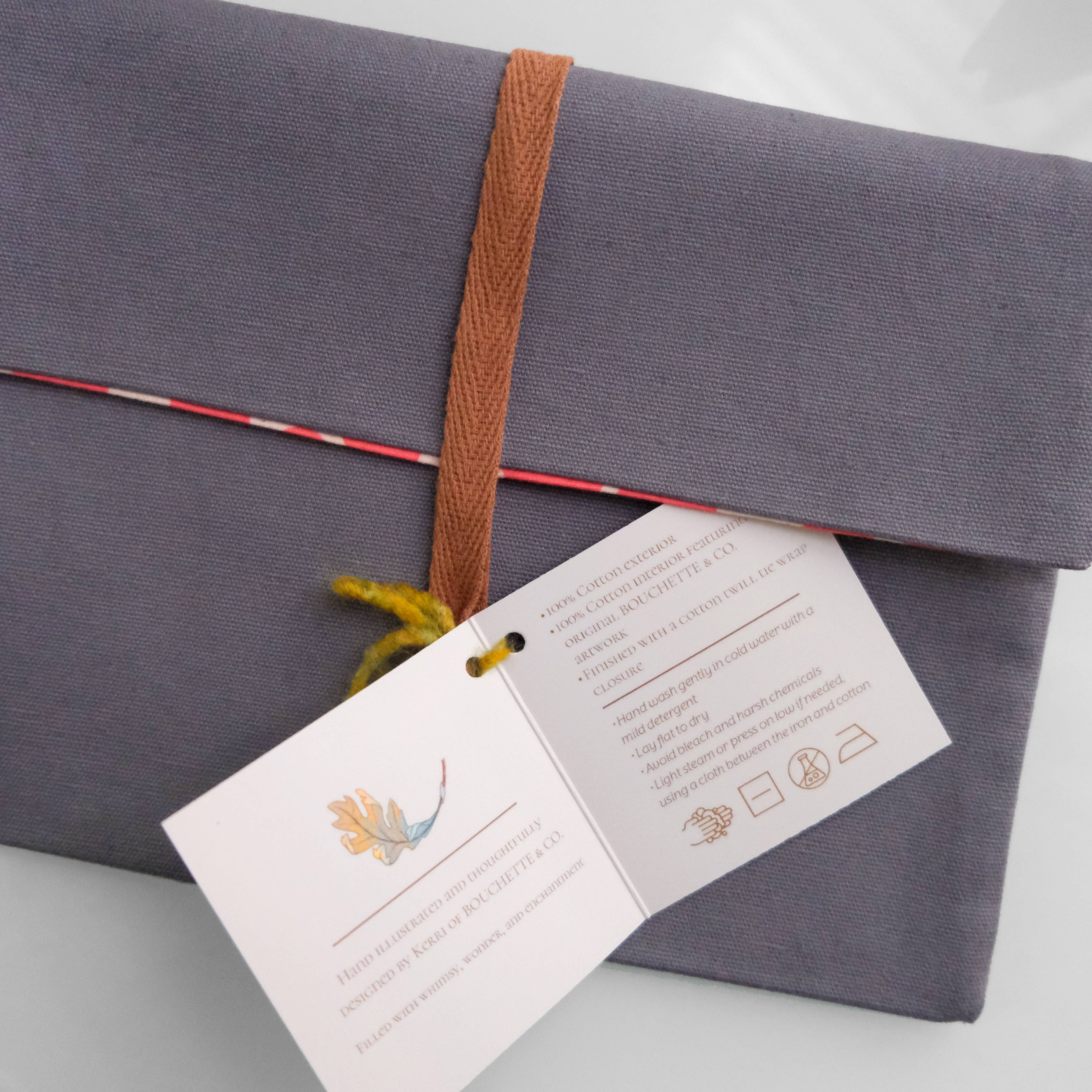 Gray fabric package with a brown ribbon and a card on a light gray background