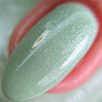 Close-up of a green glittery lip balm with a pink lip in the background