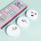 Three white bath bombs with floral designs on a light green background, next to a pink box with illustrations.
