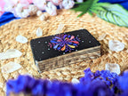 Stack of tarot cards with a colorful flower design on a woven surface with crystals and flowers.