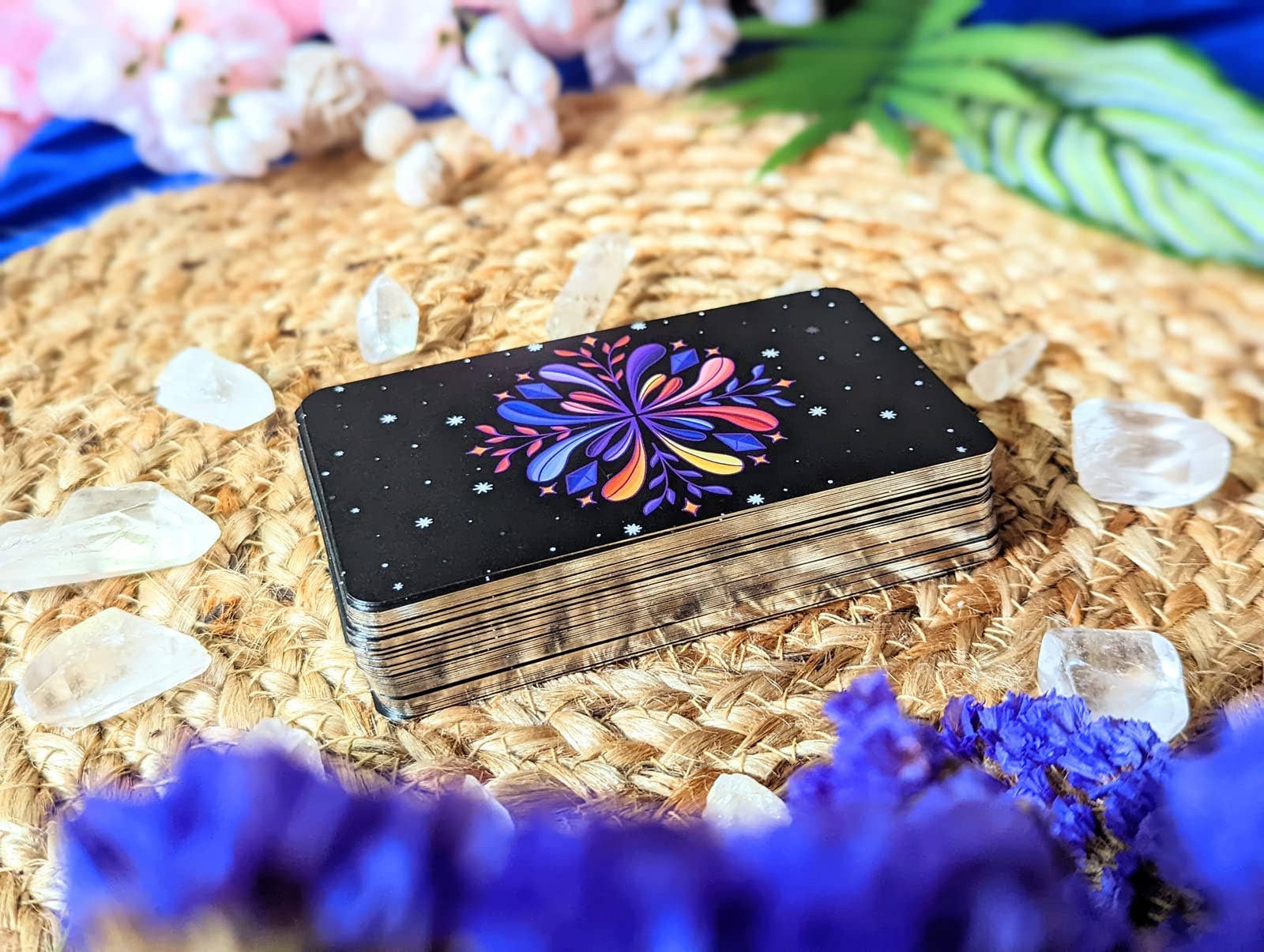 Stack of tarot cards with a colorful flower design on a woven surface with crystals and flowers.