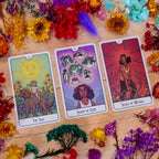 Three tarot cards on a wooden surface with flowers and feathers