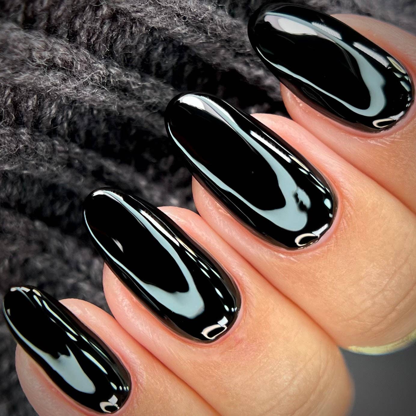 Close-up of a hand with black glossy nail polish on a textured gray background