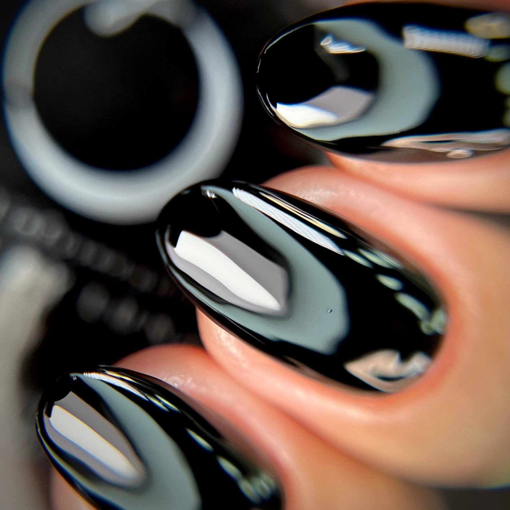 Close-up of glossy black nail polish on a person's fingernail with blurred background