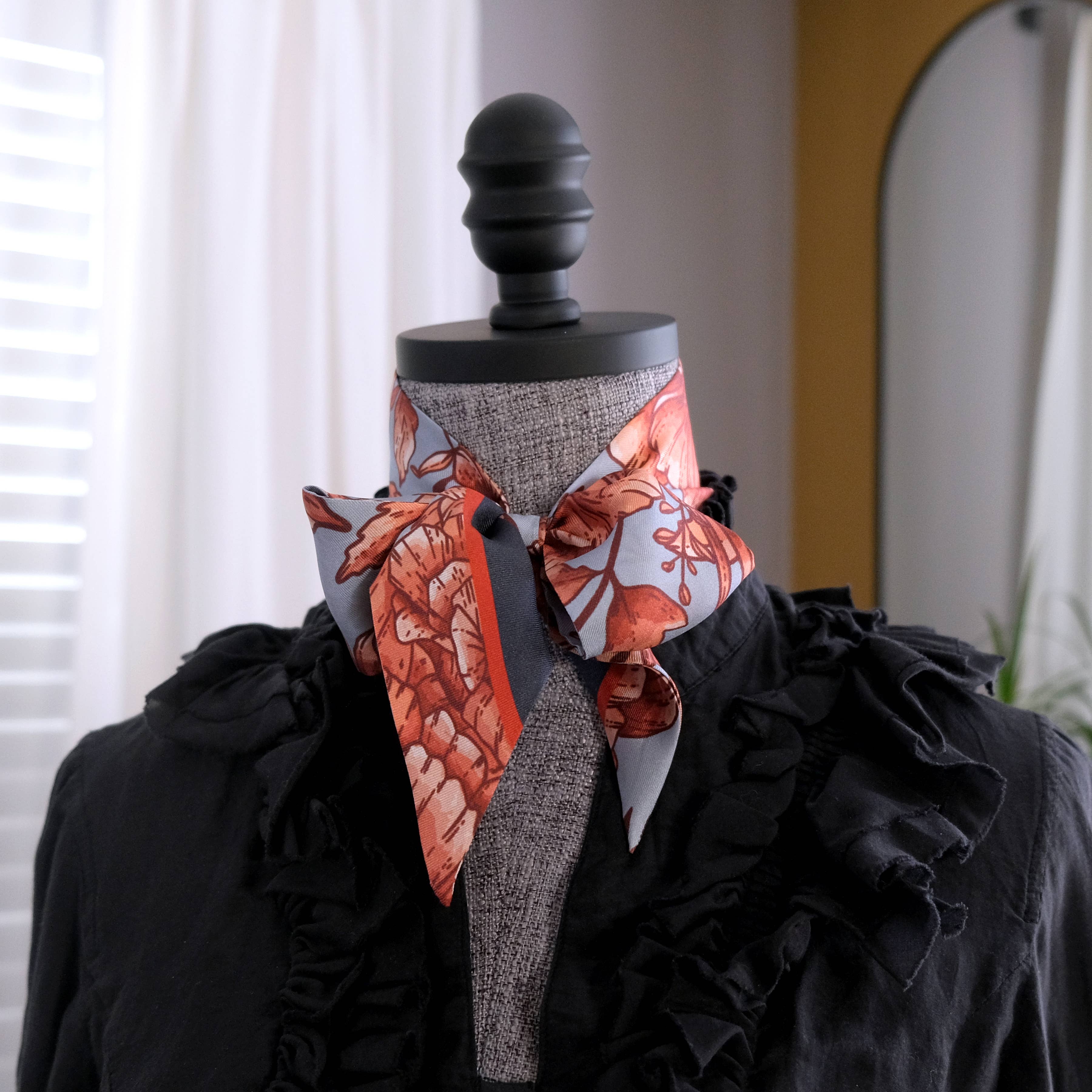 Mannequin head with a floral scarf and black garment against a neutral background