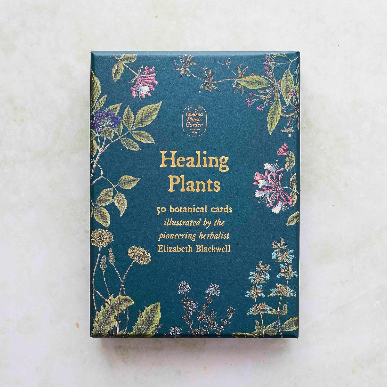 A boxed card set titled "Healing Plants" with botanical illustrations around the cover, photographed from above on a light stone-like surface. The visible text reads "50 botanical cards" and "illustrated by the pioneering herbalist Elizabeth Blackwell.