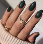 Hand with dark green nails and gold rings on a neutral background