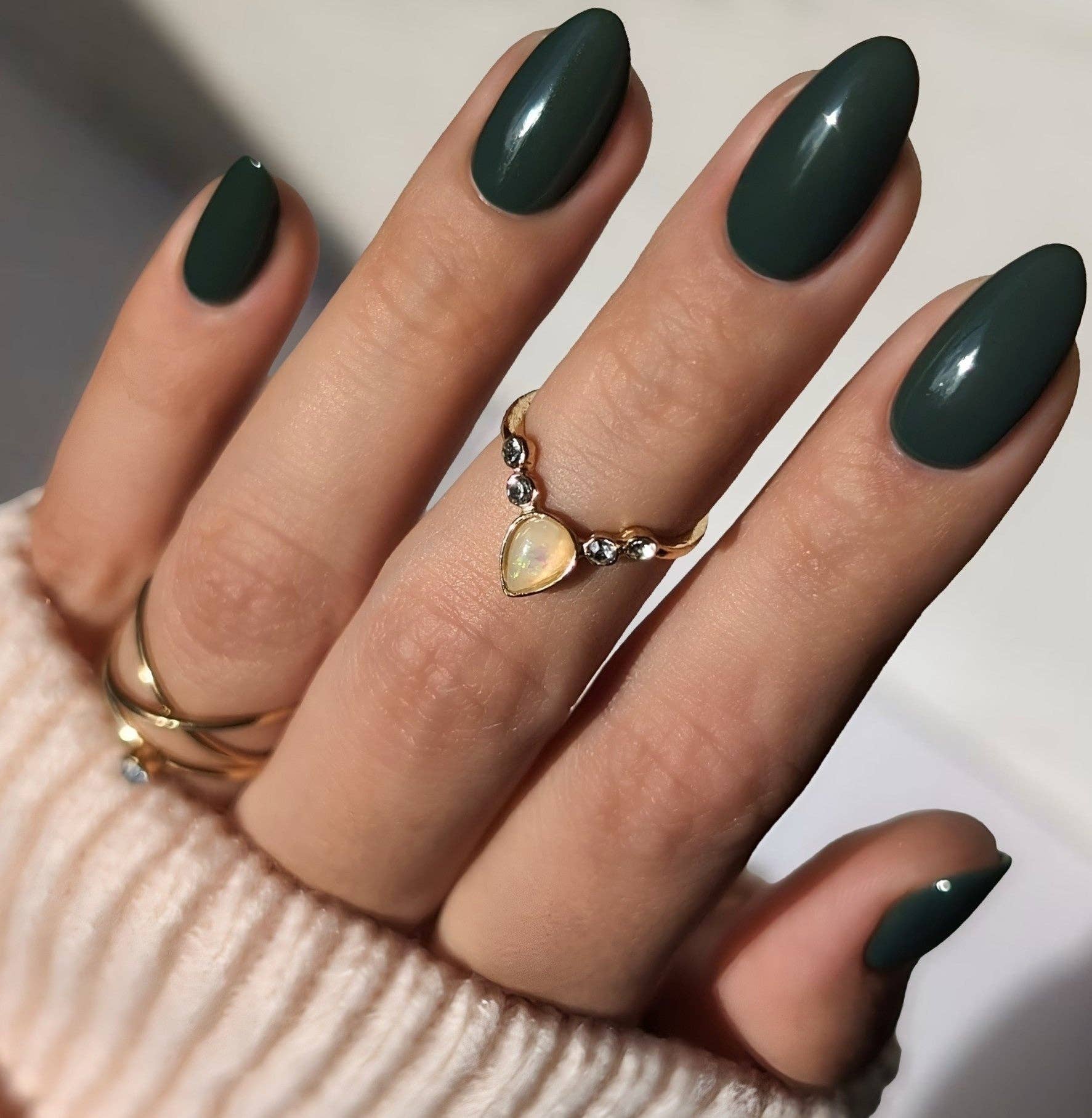 Hand with dark green nails and gold rings on a neutral background