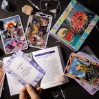 Tarot cards and book on a dark surface with a hand holding a card.