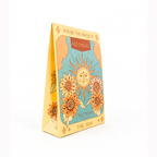 A triangular salt soap package standing upright on a white background. The package is yellow with an illustrated sun, flowers, clouds, and the text 'SON THE MAGIC', 'PATCHOLLI', 'SALT SOAP', and 'THE SUN'.
