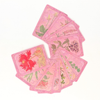 A fan arrangement of pink tarot cards displaying various botanical and floral illustrations, set against a plain white background.