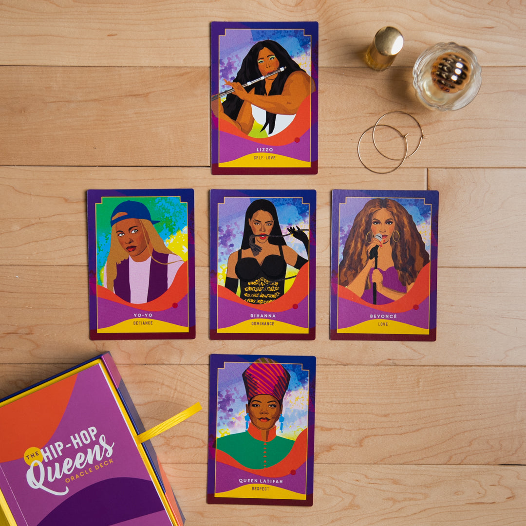 Set of colorful trading cards featuring women on a wooden surface with a box labeled 'Hip-Hop Queens'.