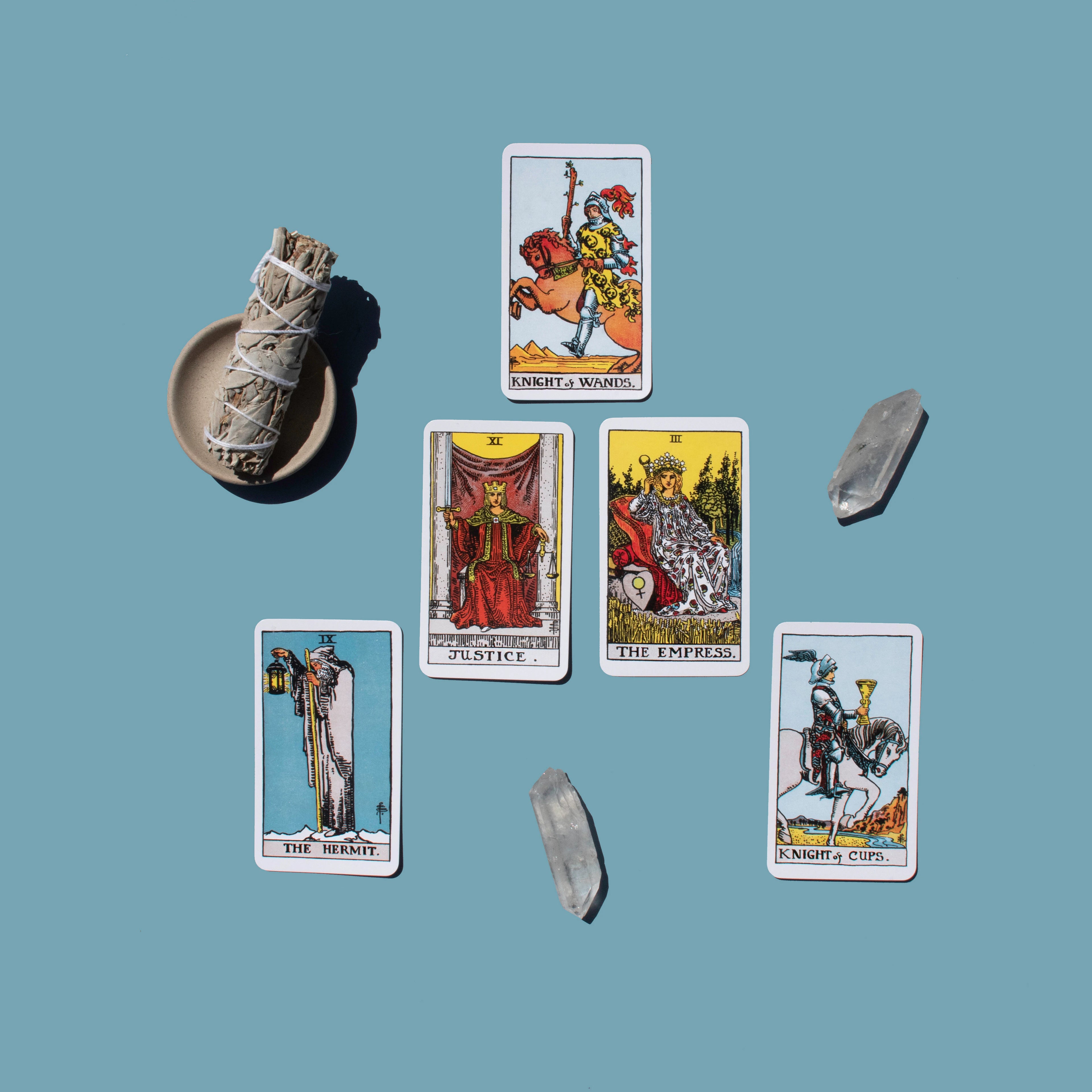 Set of tarot cards on a blue background with a smudge pot and crystals.