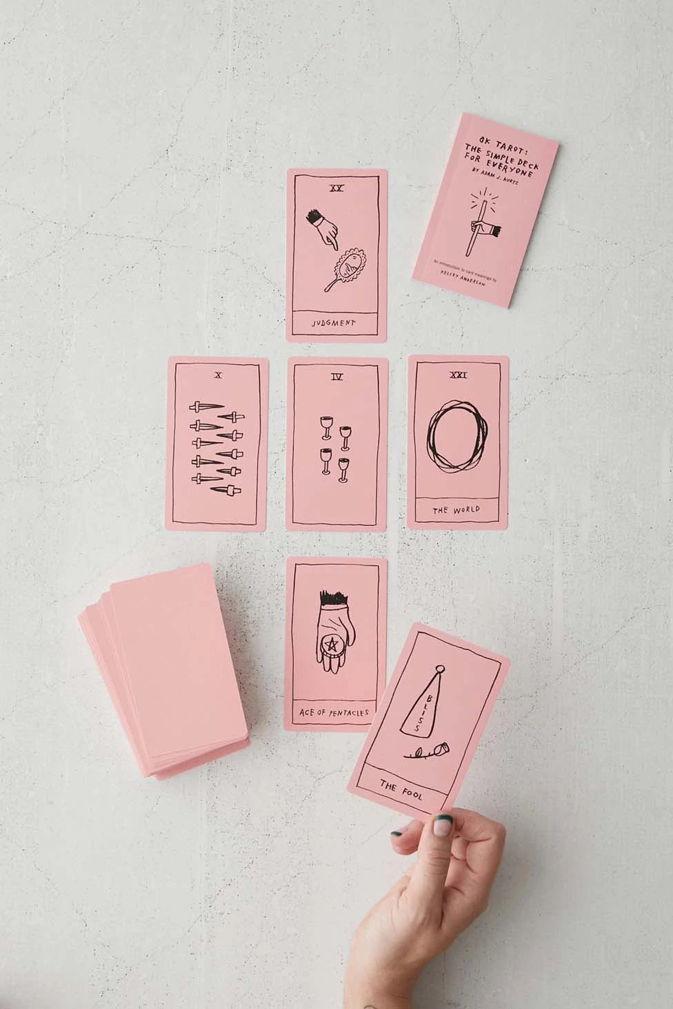 Set of pink tarot cards with black illustrations on a light gray surface.