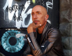 Man in a leather jacket leaning against a wall with graffiti