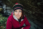 As image of the author wearing a red fleece jacket and a striped knit beanie with a red pom-pom, photographed outdoors against a dark rock face.