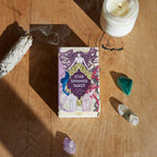 Star Spinner Tarot box on a wooden surface with a candle, crystals, and smoldering sage.