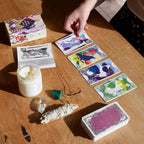 Person playing with tarot cards on a wooden table with a candle and crystals.