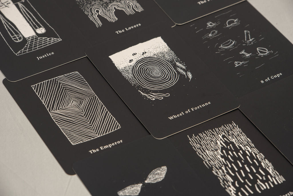 Black tarot cards with white illustrations on a light gray surface