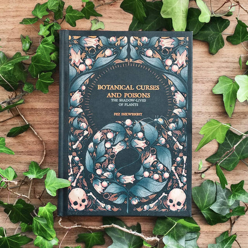 Book titled 'Botanical Curses and Poisons' surrounded by green leaves on a wooden surface