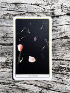 Tarot card titled 'The Void' with flowers on a wooden surface