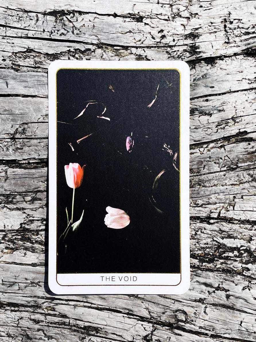 Tarot card titled 'The Void' with flowers on a wooden surface