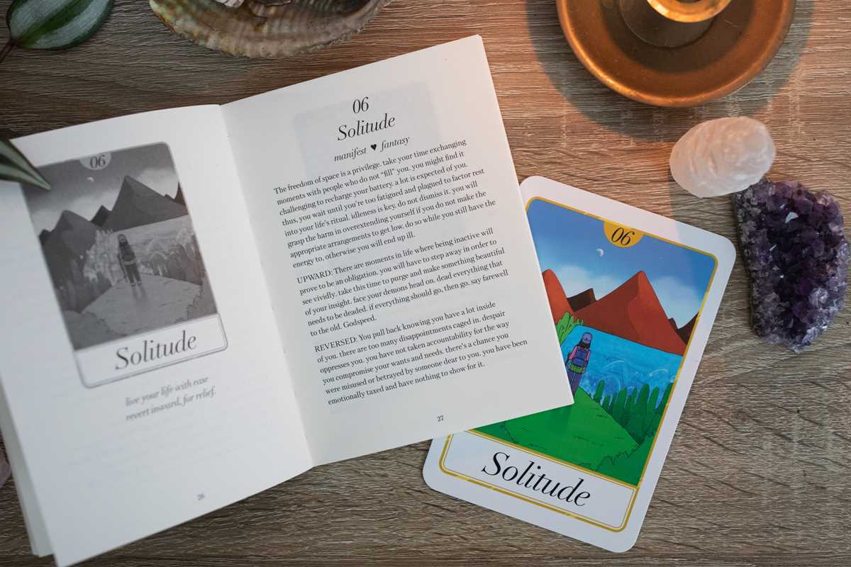 Open book with 'Solitude' card on a wooden surface with crystals and a candle.