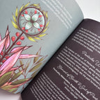 An open book showing two interior pages with printed text and a large floral illustration. The left page has a pale blue-gray background with pink, green, and yellow botanical artwork, and the right page is dark charcoal with black text.