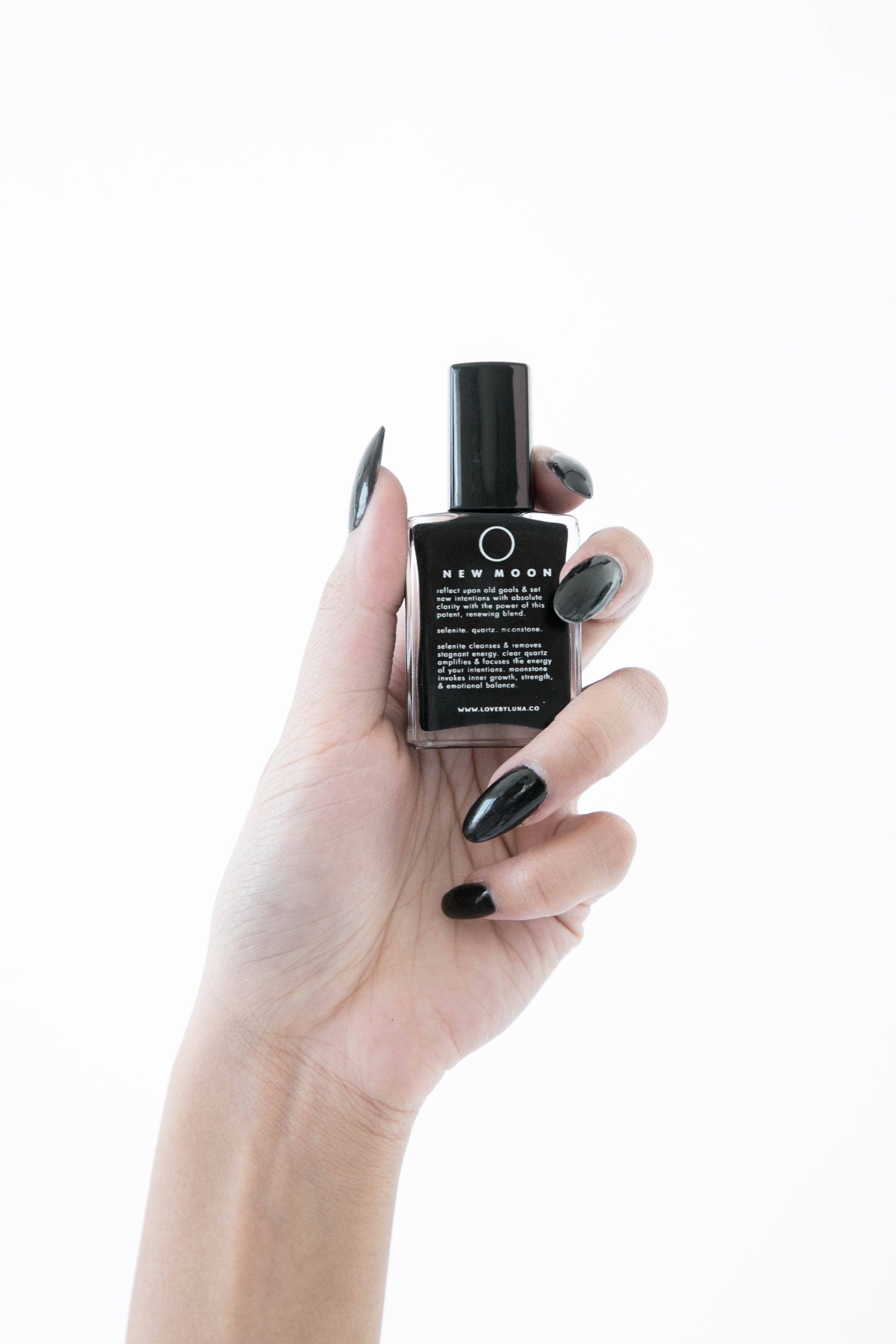 Hand holding a black nail polish bottle labeled 'New Moon' against a white background