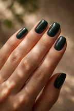 Hand with dark green nail polish against a blurred natural background