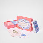 A boxed deck of playing cards called REGENCY, shown with its coral-pink box, an open pink drawer-style box, a blue-backed card deck standing upright, and two sample cards in front on a clean white studio background.