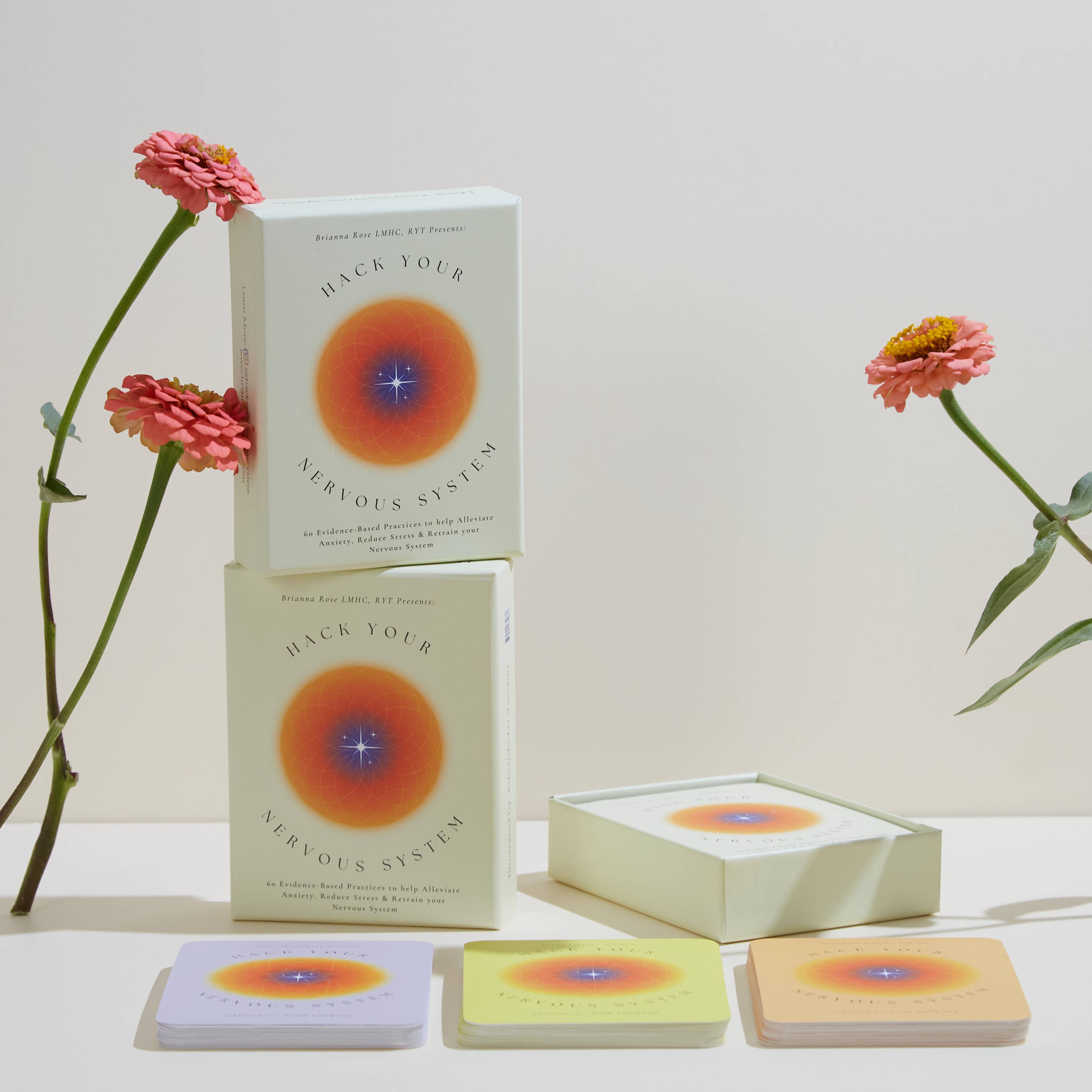 Books and card decks titled 'Hack Your Nervous System' with flowers on a light background