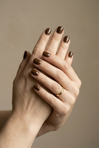 Close-up of two hands with dark nail polish against a beige background