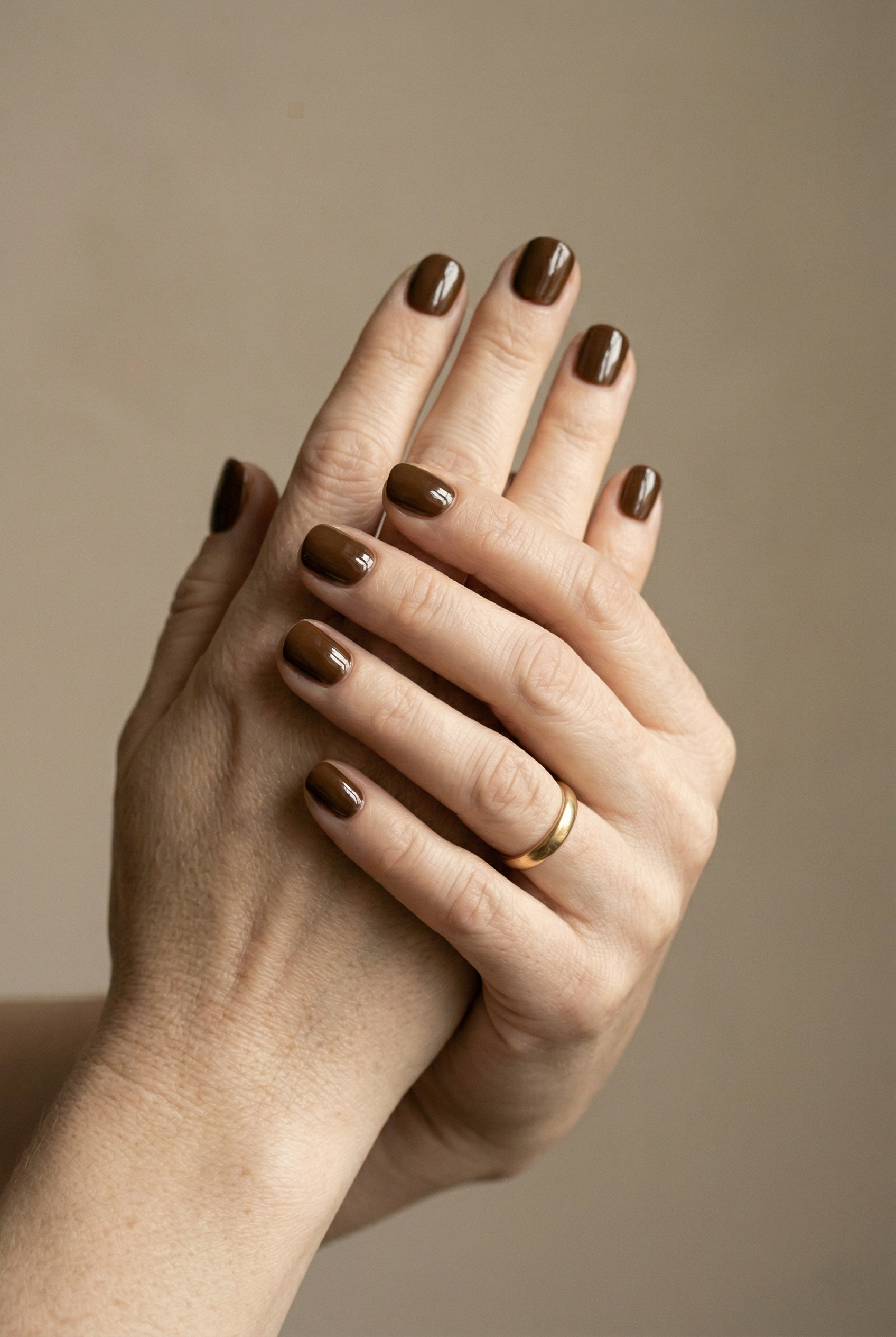 Close-up of two hands with dark nail polish against a beige background