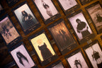 A close-up of multiple tarot cards arranged on a wooden surface. The cards have dark borders and sepia-toned illustrations of ghostly, eerie, and gothic figures, with titles like 'The Witch', 'The Dead', and 'The Moon' visible.