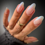 Hand with long, gradient nails wearing a gold ring on a dark background