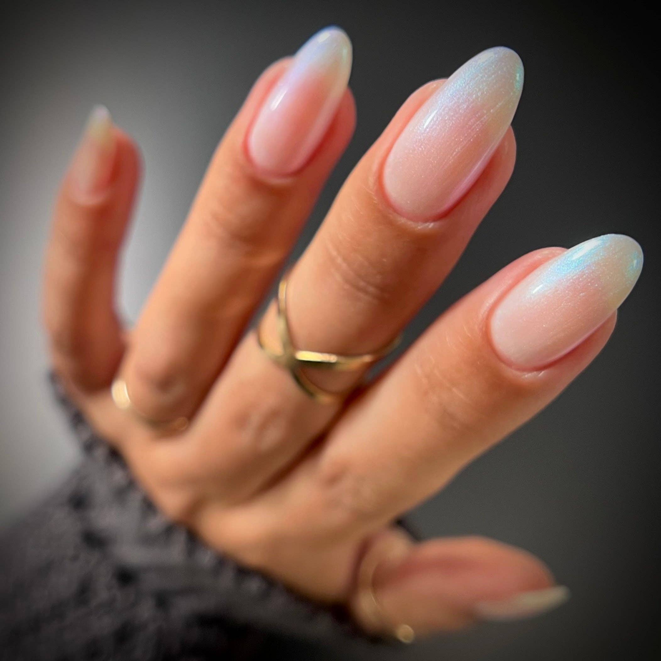 Hand with long, gradient nails wearing a gold ring on a dark background