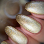 Close-up of a hand with gold glittery nail polish on a blurred background