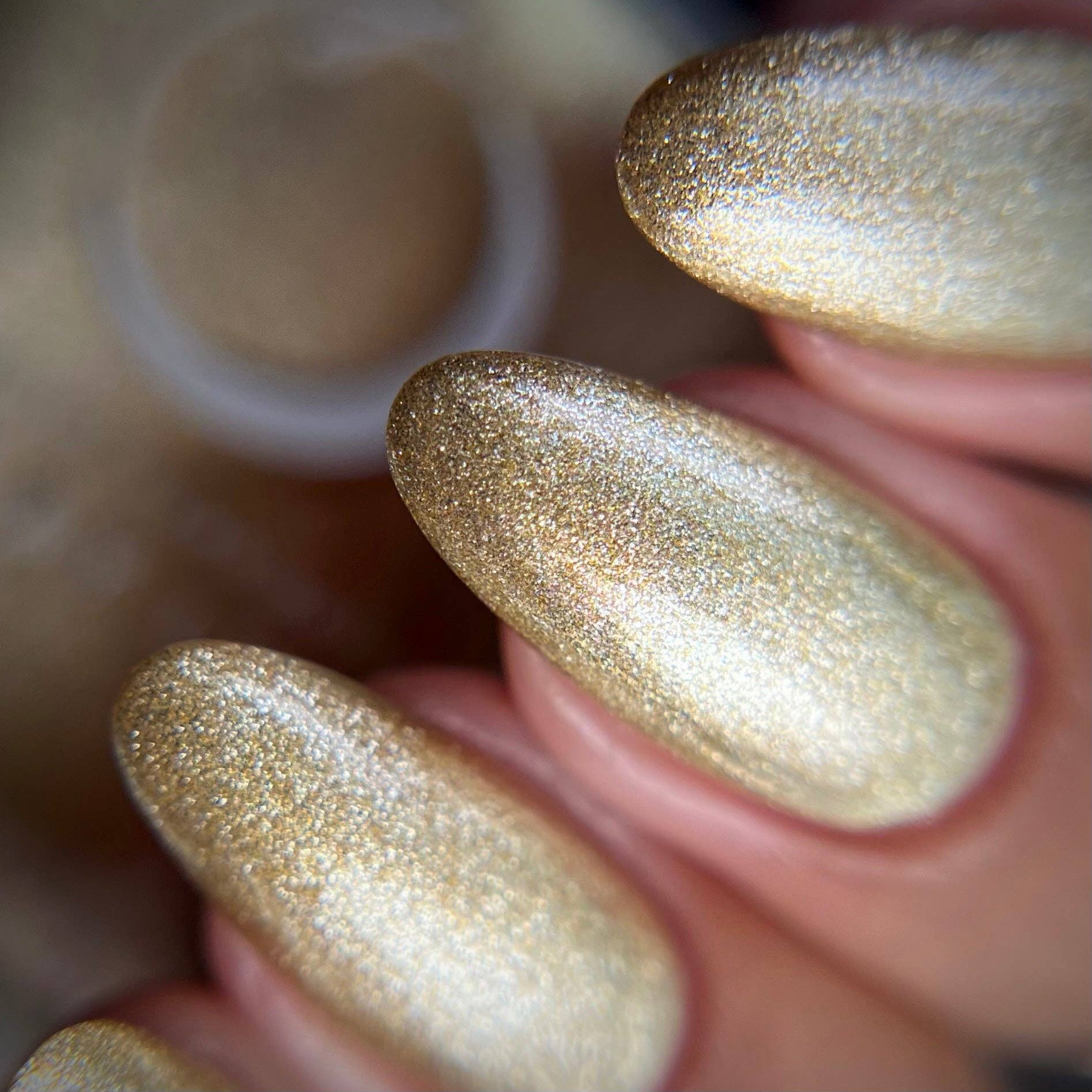 Close-up of a hand with gold glittery nail polish on a blurred background